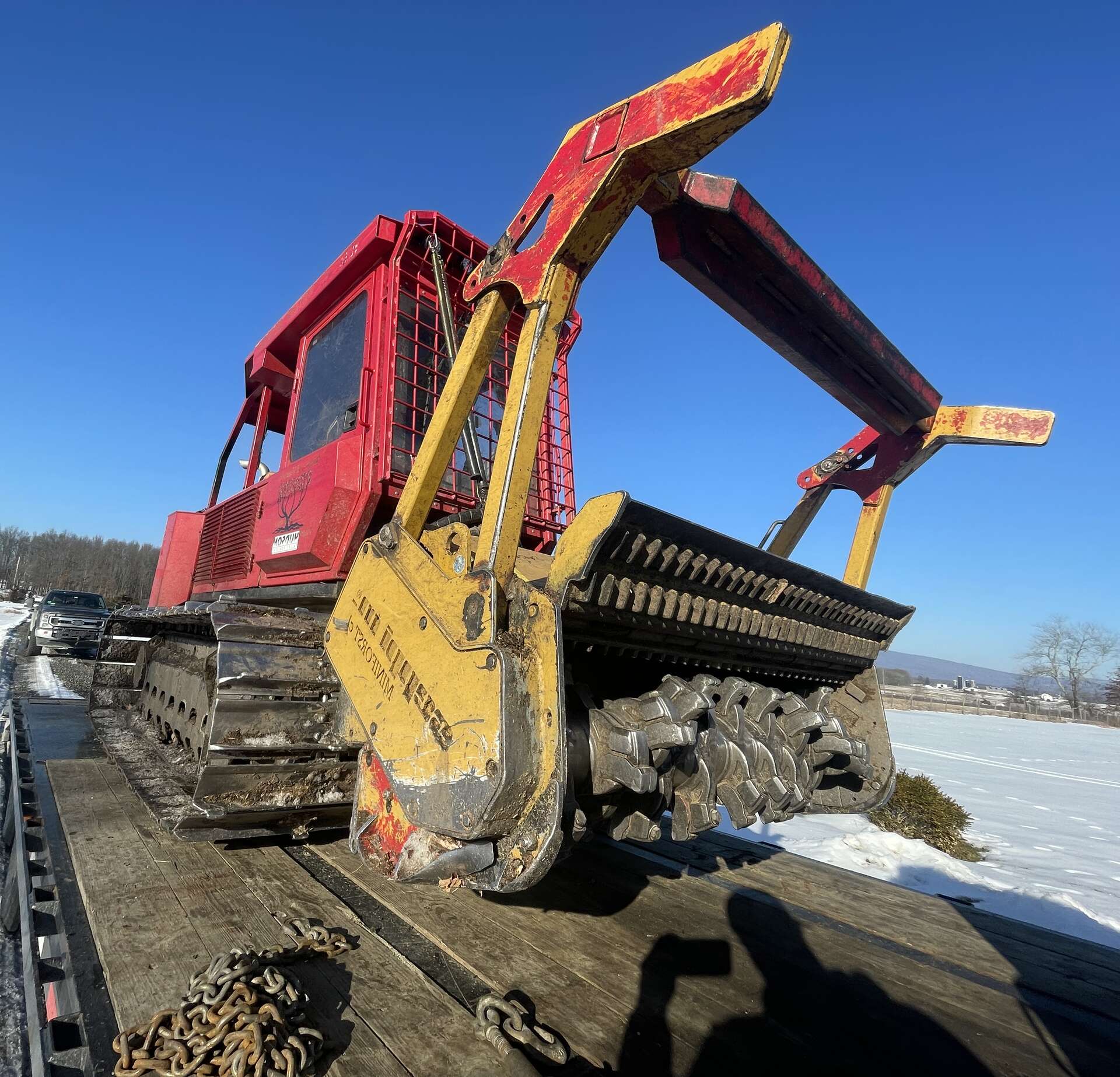 Hudson Valley Forestry tracked mulcher with raised head, chained down on a flatbed under a winter sky